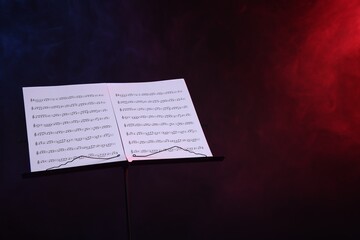 Stand with music sheets on dark background with smoke, space for text