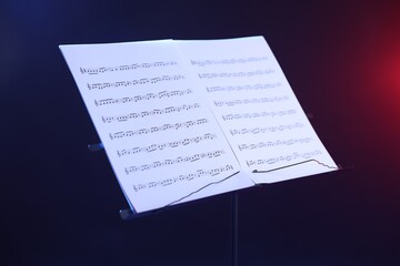 Stand with music sheets in neon lights on dark background, closeup