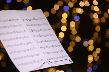 Note stand with music sheets against blurred lights, closeup. Space for text
