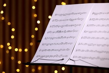 Note stand with music sheets against blurred lights, closeup. Space for text