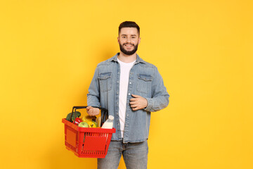 Man with shopping basket full of products on orange background