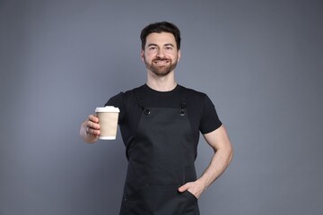 Portrait of smiling barista with paper takeaway cup of hot drink on grey background