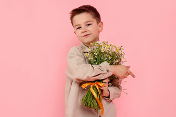Portrait of cute little boy with bouquet of beautiful chamomile flowers on pink background