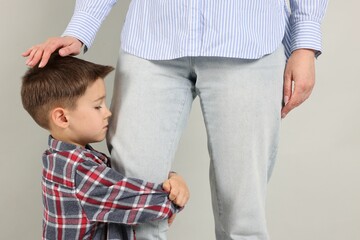 Little boy afraid to leave without mother and hugging her on grey background. Separation anxiety
