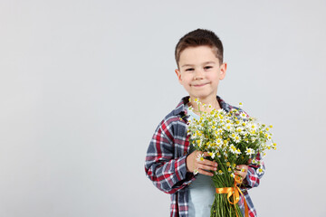 Portrait of cute little boy with bouquet of beautiful chamomile flowers on light grey background....