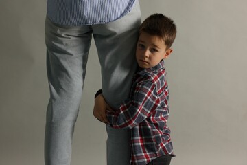 Little boy afraid to leave without mother and hugging her on grey background. Separation anxiety