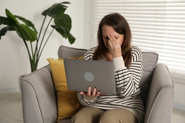 Woman with vision problem using laptop in armchair at home