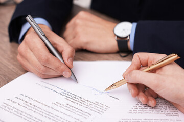 Woman pointing at document and man putting signature at table, closeup