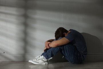 Teen problems. Upset teenage boy near light wall indoors, space for text