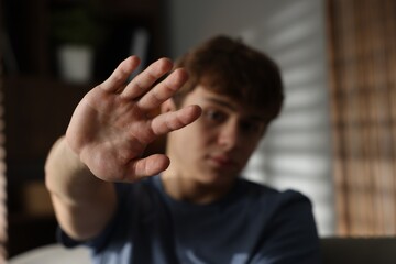 Teen problems. Upset teenage boy making stop gesture at home, selective focus
