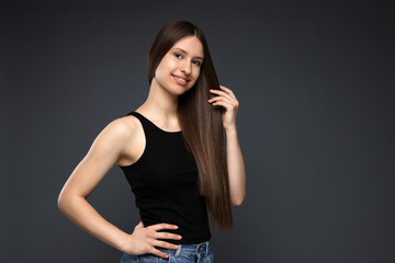 Fototapeta premium Portrait of smiling teenage girl with healthy long hair on dark grey background