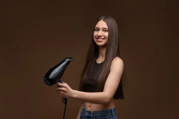 Fotobehang Smiling teenage girl with hair dryer on brown background © New Africa
