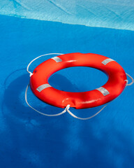 Closeup view of bright red lifebuoy floating in clear blue pool water. Strong summer safety...