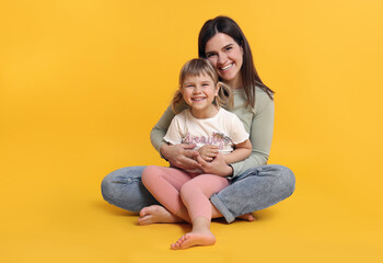 Happy mother and her cute daughter on orange background