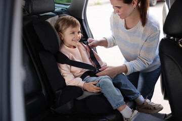 Happy mother fastening her daughter in child safety seat inside car