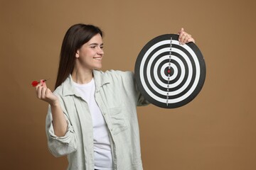 Targeting. Smiling woman with dart board and arrow on beige background