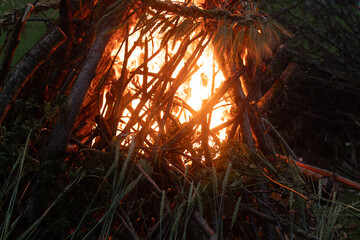 A dark, moody image of a bonfire made of thick branches and adorned with a wreath of braided grain,...