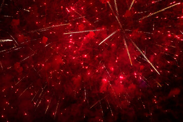 Bright red fireworks burst across dark sky with scattered glowing trails and sparkles, creating...