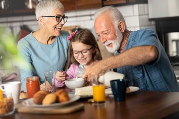 Happy grandchildren girl having breakfast with her grandparents.
