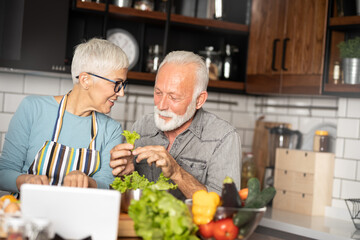 Mature couple cooking together in kitchen, using tablet for recipe guidance. Seniors, lifestyle, technology, bonding