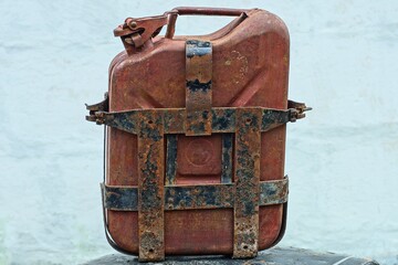 one closed lid retro brown with handle iron fuel industrial old motorcycle in case with plates canister stands on table near white wall day outside