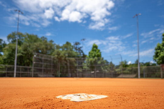 Detailed view of a baseball field with second base in focus under a bright blue sky during daytime - Powered by Adobe