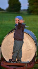 Toddler boy standing on a garden watering tank in the countryside on a sunny day. Playful rural...