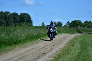 Motorcyclist rides an adventure touring motorcycle on a gravel countryside road. Rural landscape...