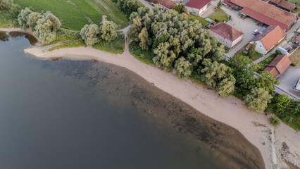 Ruhiger Flusslauf mit Sandstrand und Bäumen in Nähe eines kleinen Dorfes