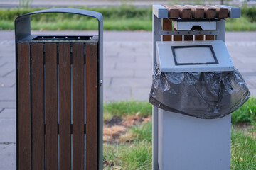Close-up view of two different styles of public trash bins positioned on a sidewalk in a green...