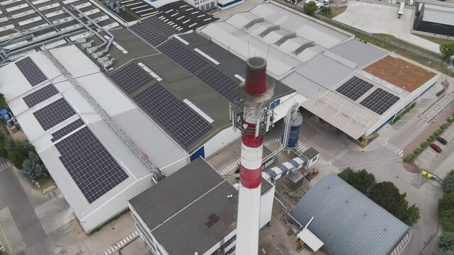 Smoking chimney of a modern factory with solar panels on roof. Ecology with renewable energy sources in furniture industry. Trnava, Slovakia