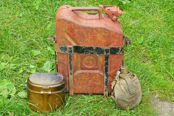 one closed lid retro brown with handle iron fuel industrial old motorcycle in case with plates canister stands with military flask and soldier's camp mess tin stand on green grass outside