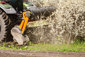 Picture of a tractor-type truck working on clearing bushes with a certain device. It is a sunny day...