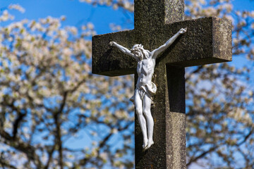 Beautiful Jesus Christ on crucifix, spring Easter budding tree flowers in background, cemetery on a...