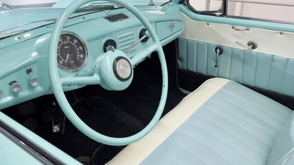 Close-up of a retro car interior in turquoise and cream tones. Classic dashboard, steering wheel, and leather seats evoke nostalgic mid-century automotive de