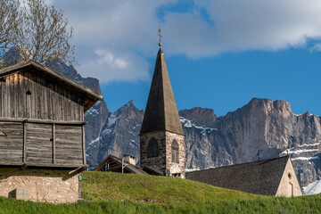 Close-up view of Santa Maddalena Church in the green valley of South Tyrol with forested hills in the background.