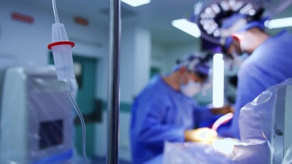 Drop counter with saline solution. Close up. Two male surgeons operate patient at blurred backdrop. - Powered by Adobe