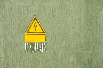 A yellow sign with a lightning bolt on it is stuck to a green wall