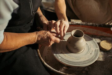 Potter carefully shaping clay on pottery wheel with senior woman