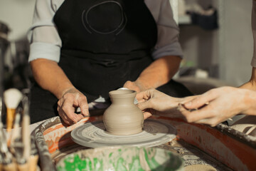 Potter assisting senior woman creating clay vase on pottery wheel