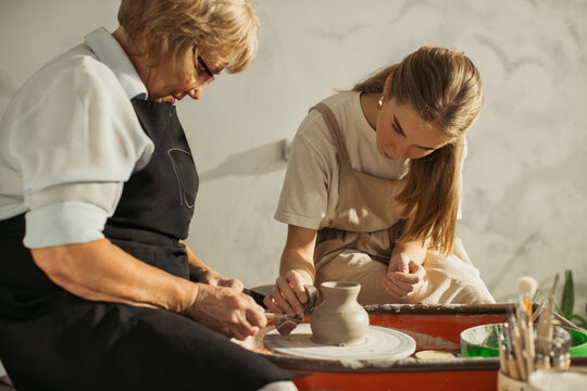 Senior potter teaching apprentice clay modeling on pottery wheel