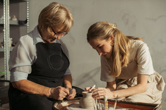 Experienced and young craftswomen creating pottery together in workshop