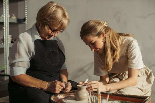 Senior and young women creating pottery together in workshop