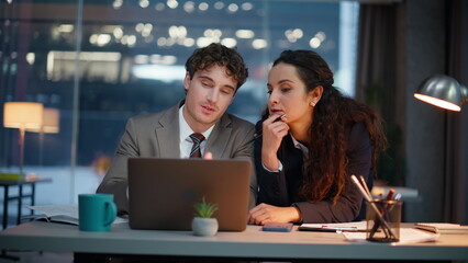 Late workers looking computer screen at night office closeup. Flirting man woman