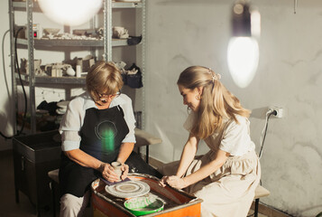 Senior and young women creating pottery on spinning wheel in workshop