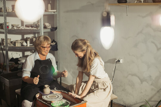 Senior potter teaching apprentice how to use pottery wheel