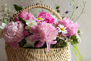 A bouquet of peonies with wild flowers in a basket on a light background, close-up