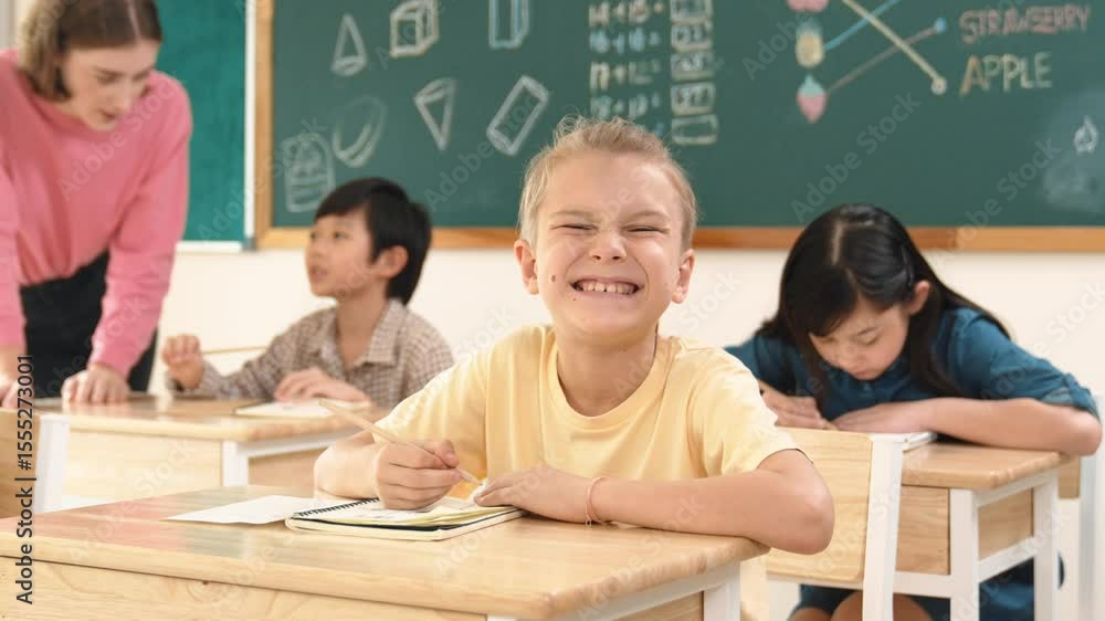 Aufkleber caucasian smart child smiling at camera while doing classwork at classroom while happy multicultural