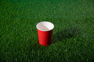 Paper cup stands on artificial grass with blue background from behind
