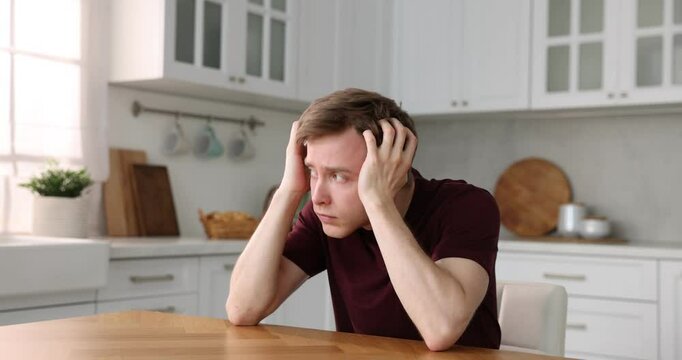 Paranoia. Worried man looking around at wooden table in kitchen